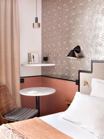 Ein Hotelzimmer mit einem Bett, einem runden Tisch, einem Sessel, einem Bücherregal und einer Wandleuchte.