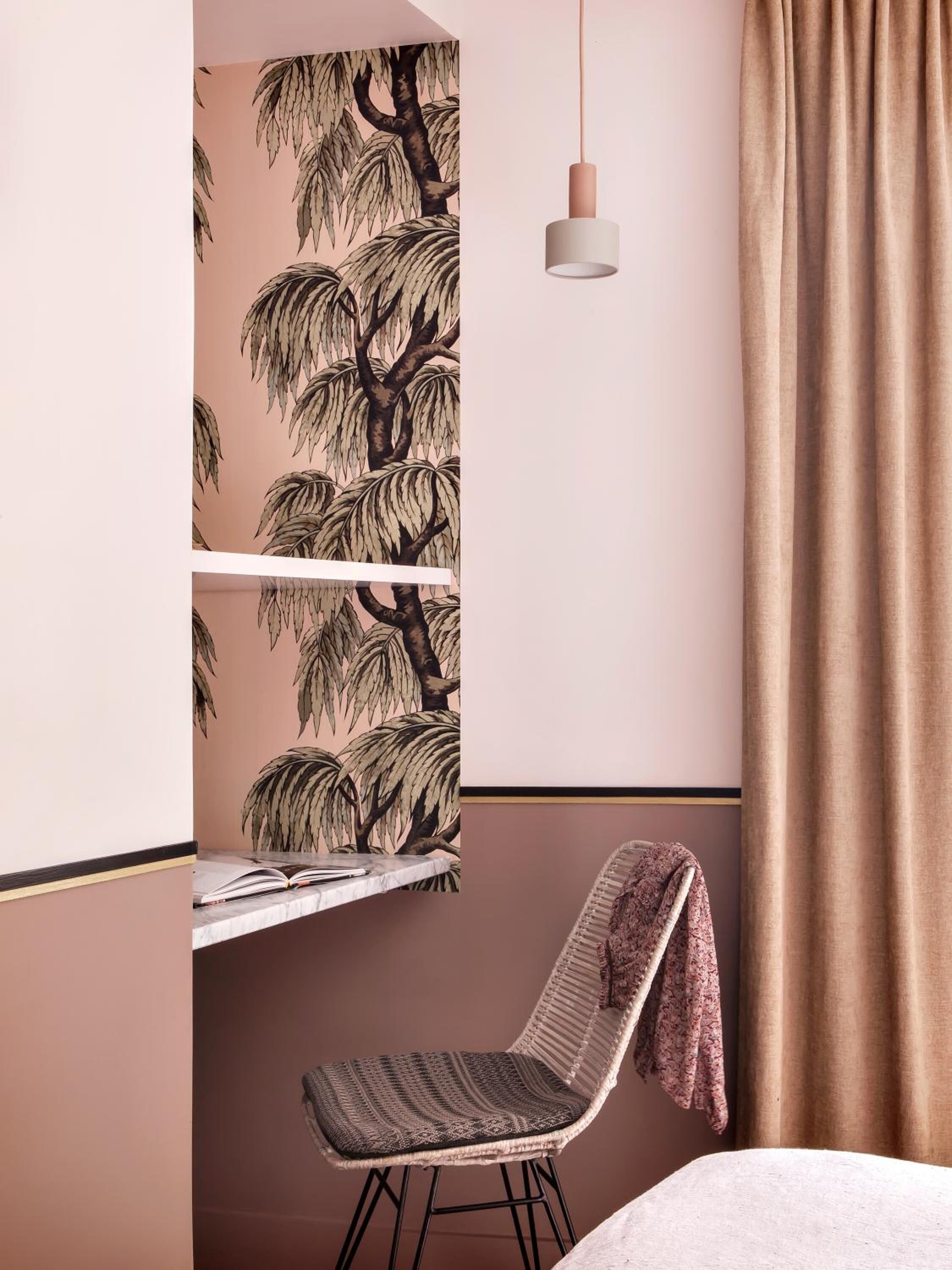 A room with a bed, a chair with a blanket, a hanging light, and a wall with a tree pattern.