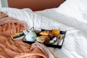 A tray with croissants, juice, jam, and a teapot on a bed with white linens.