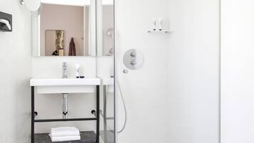 A modern bathroom with a glass-enclosed shower, a white sink with a mirror, and a marble-tiled floor.