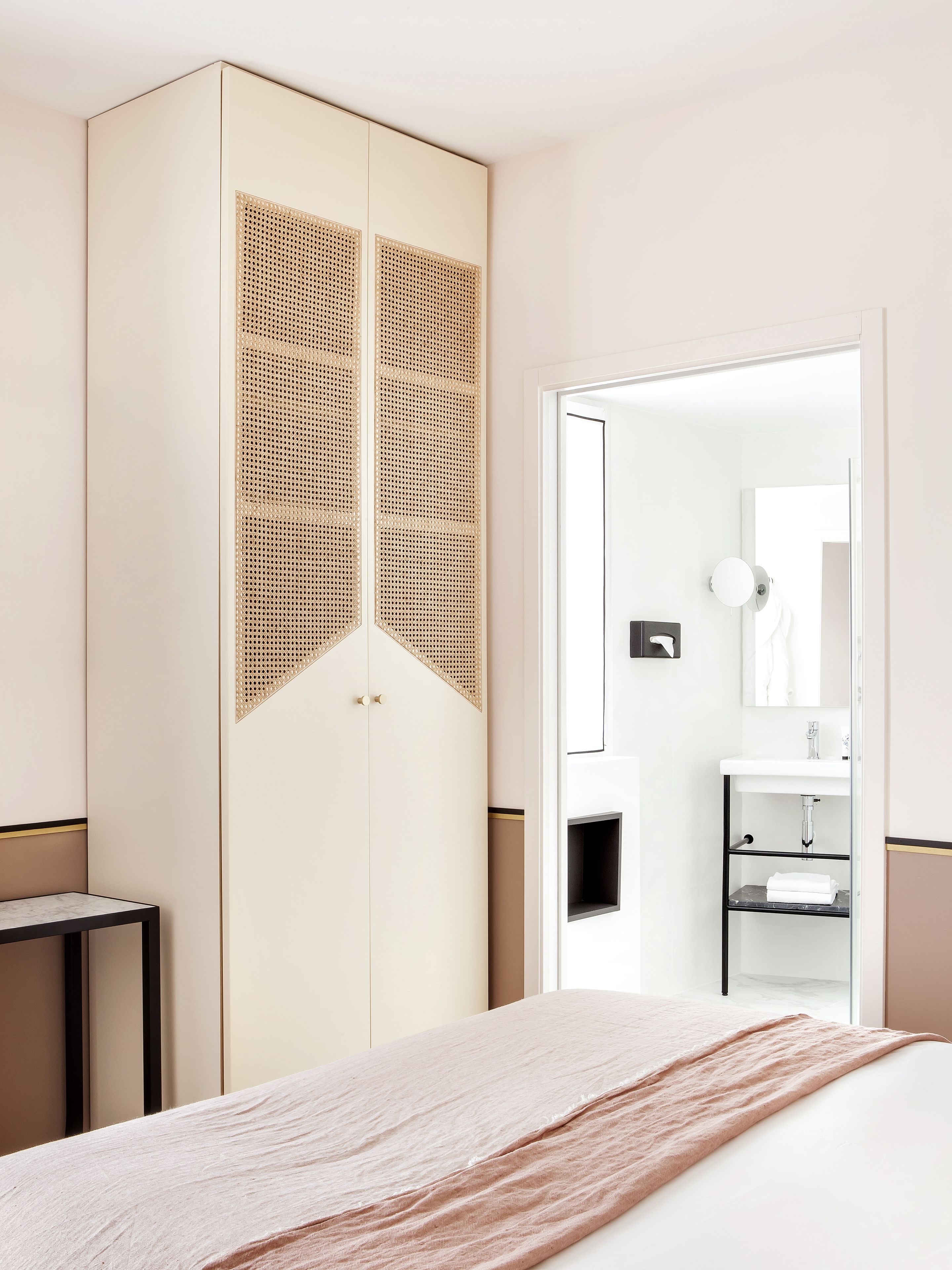 Un dormitorio con cama, armario, mesita de noche y baño visible a través de una puerta abierta.