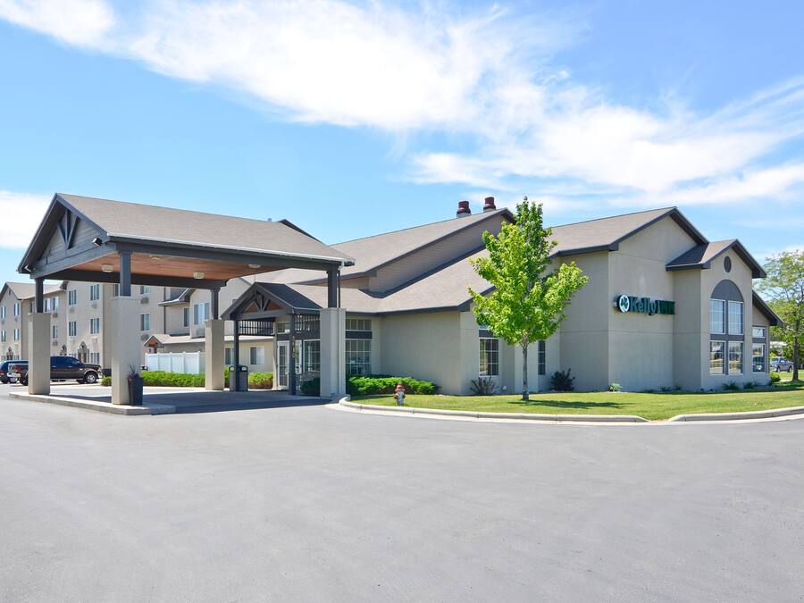 A modern hotel with a covered entrance, large windows, and a landscaped lawn.