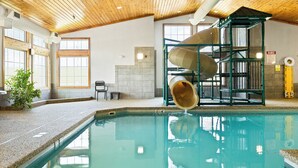 Ein beheizter Innenpool mit Holzbalkendecke, einer Wasserrutsche und einem Liegestuhl am Pool.