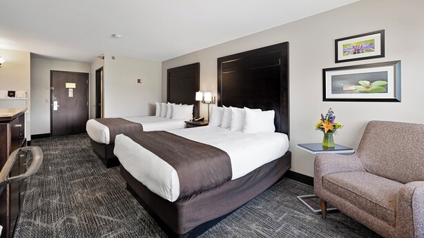 Ein Hotelzimmer mit zwei Betten, einem Schreibtisch, einem Stuhl und einem kleinen Tisch mit Blumen.