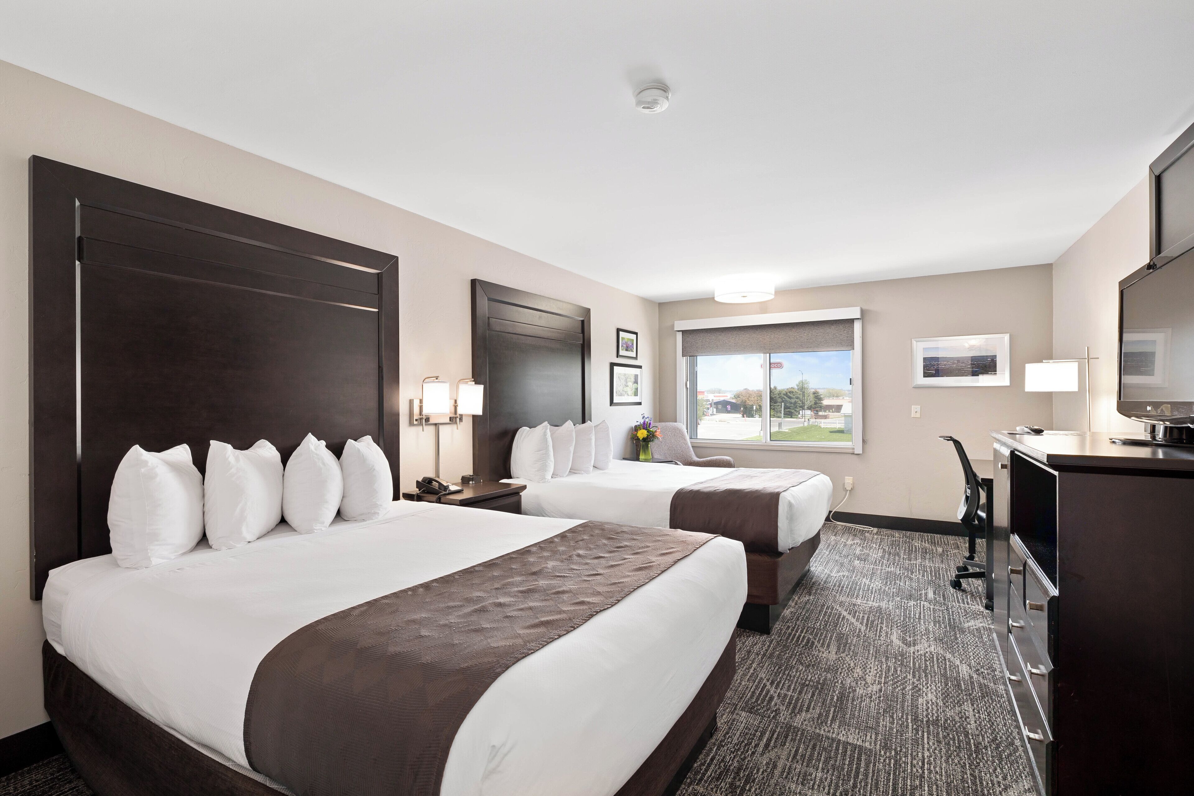 A hotel room with two beds, a desk, a TV, and a window with a view.