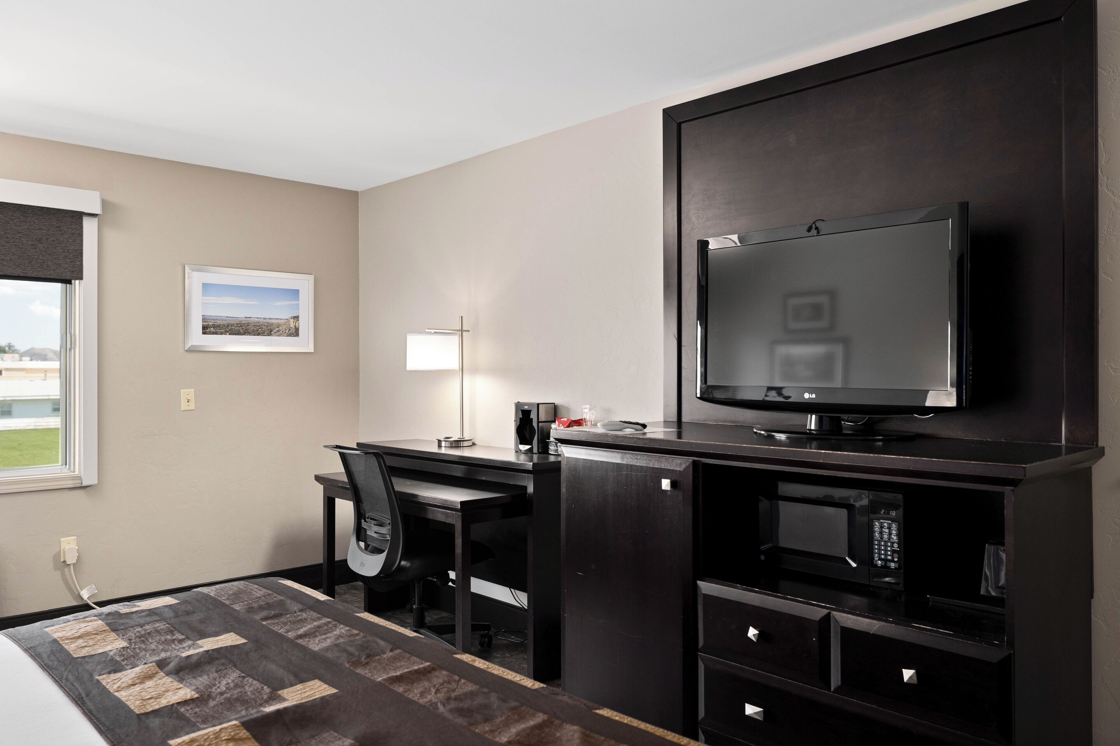 Une chambre d’hôtel comprenant un lit, un bureau avec une chaise, une télévision, un four à micro-ondes et un petit réfrigérateur.