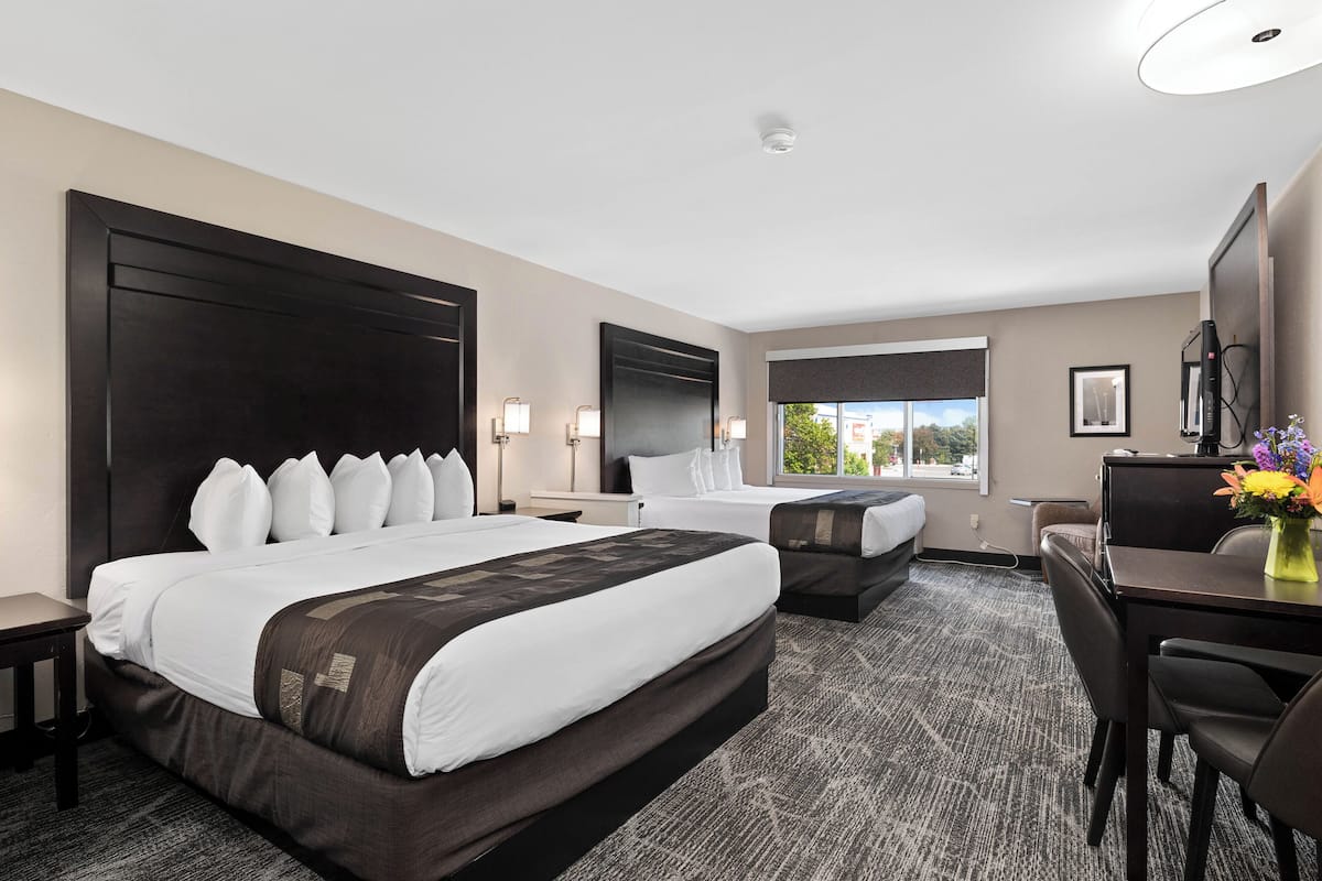 A hotel room with a large bed, a smaller bed, a desk, a chair, and a window with a view of the outdoors.