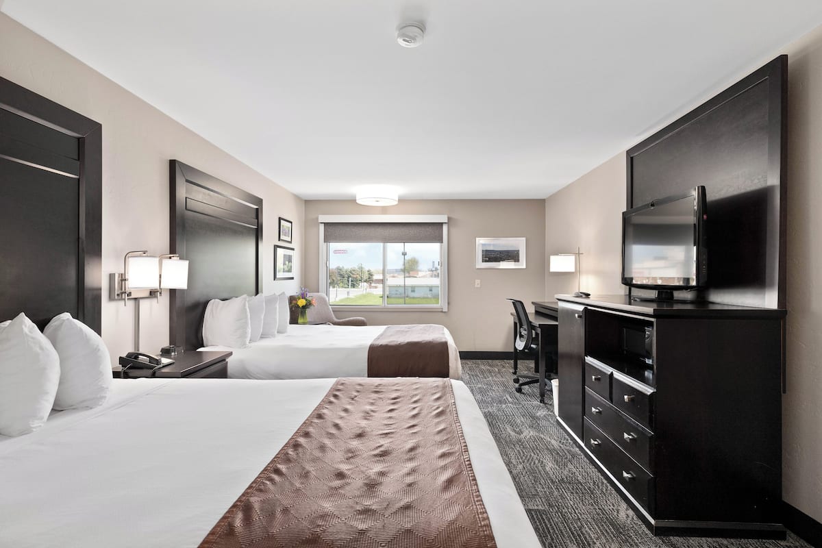 A hotel room with two beds, a desk, a television, and a view of the outdoors.