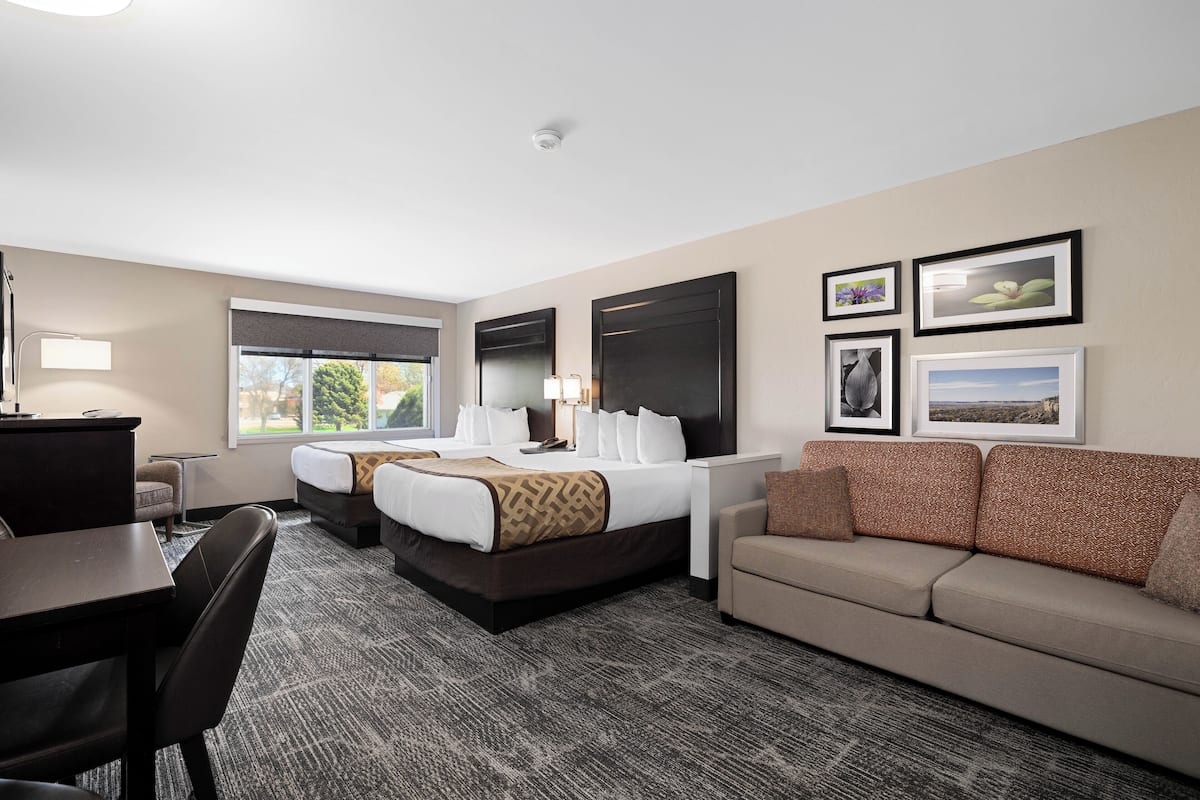 A hotel room with two beds, a desk, a sofa, and a carpeted floor.