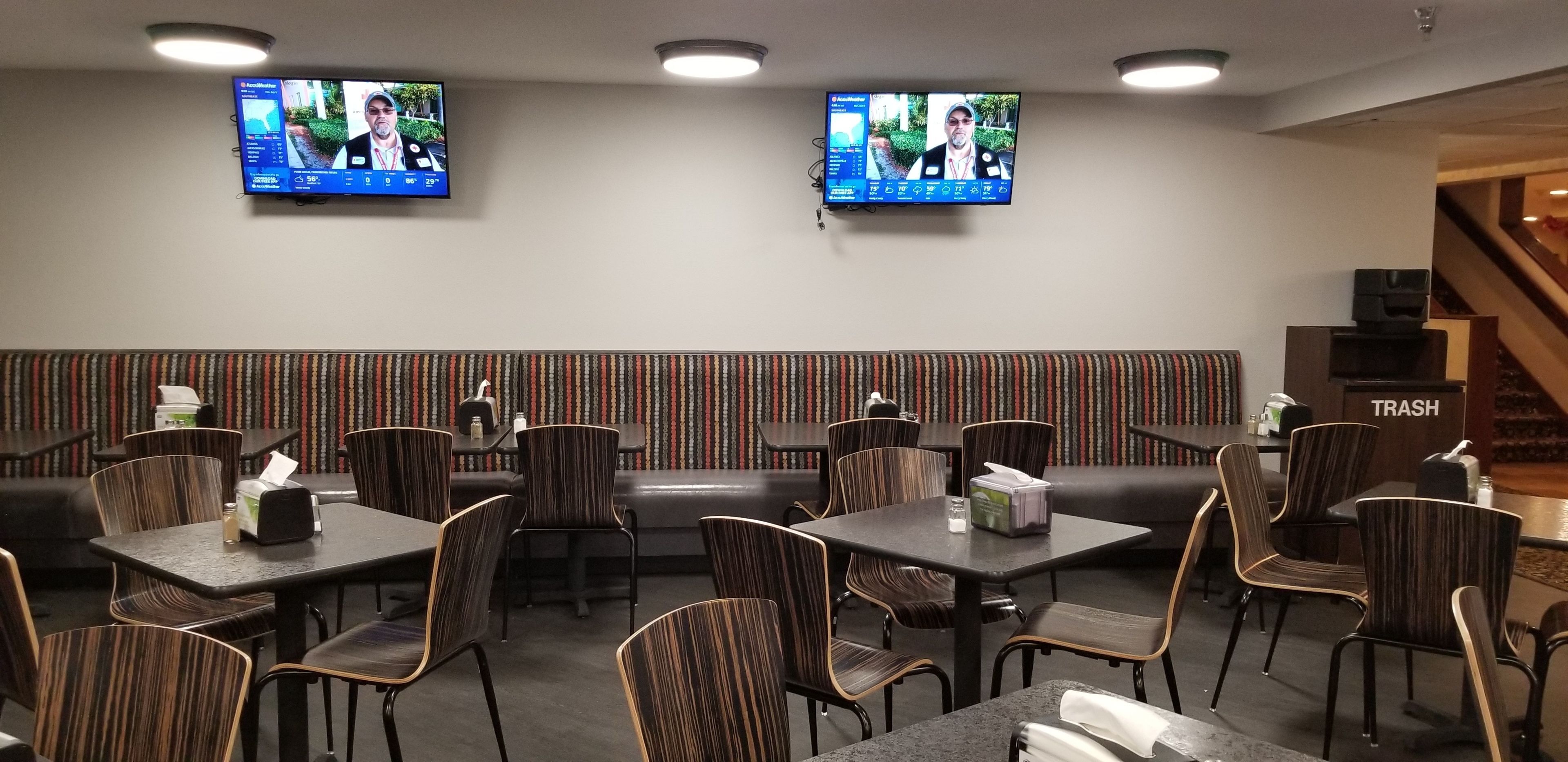 En restaurang med flera bord och stolar, två tv-apparater som hänger på väggen och ett väggmönster med ränder.