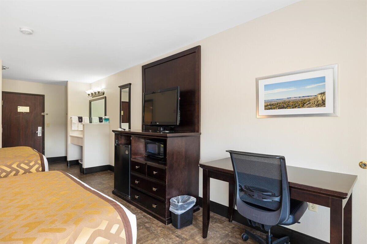 A hotel room with a bed, a desk with a chair, a TV, a trash bin, and a framed picture on the wall.