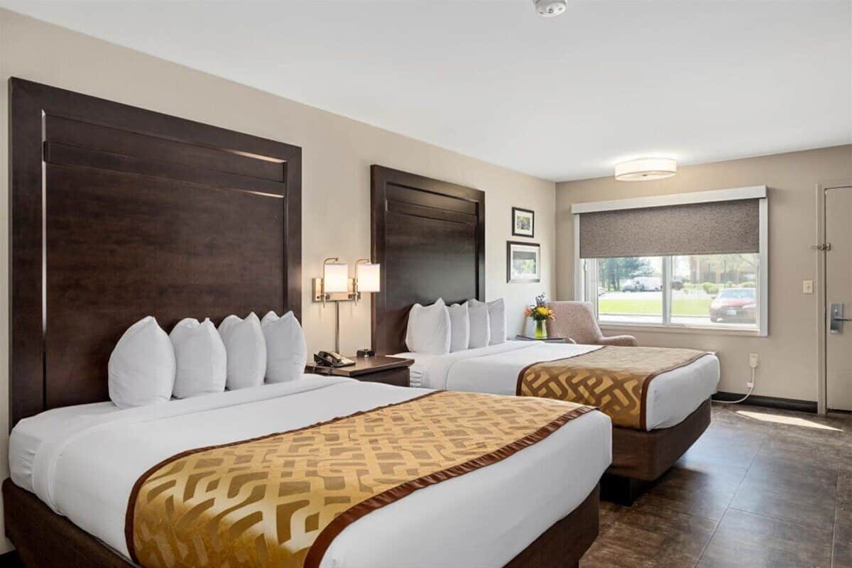 A hotel room with two beds, a large window, and a view of the outside.