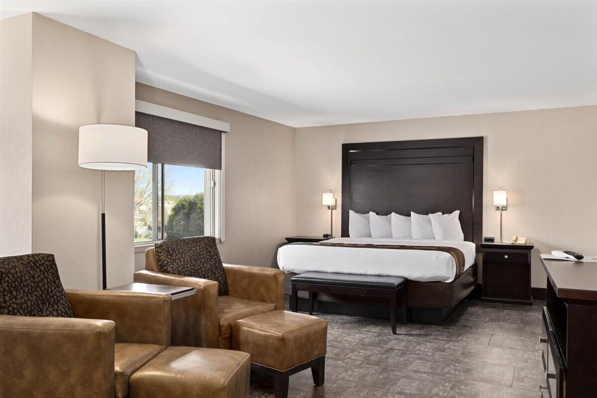 Habitación de hotel con una cama grande, dos mesitas de noche, un escritorio y una zona de estar con sillas y un banco.