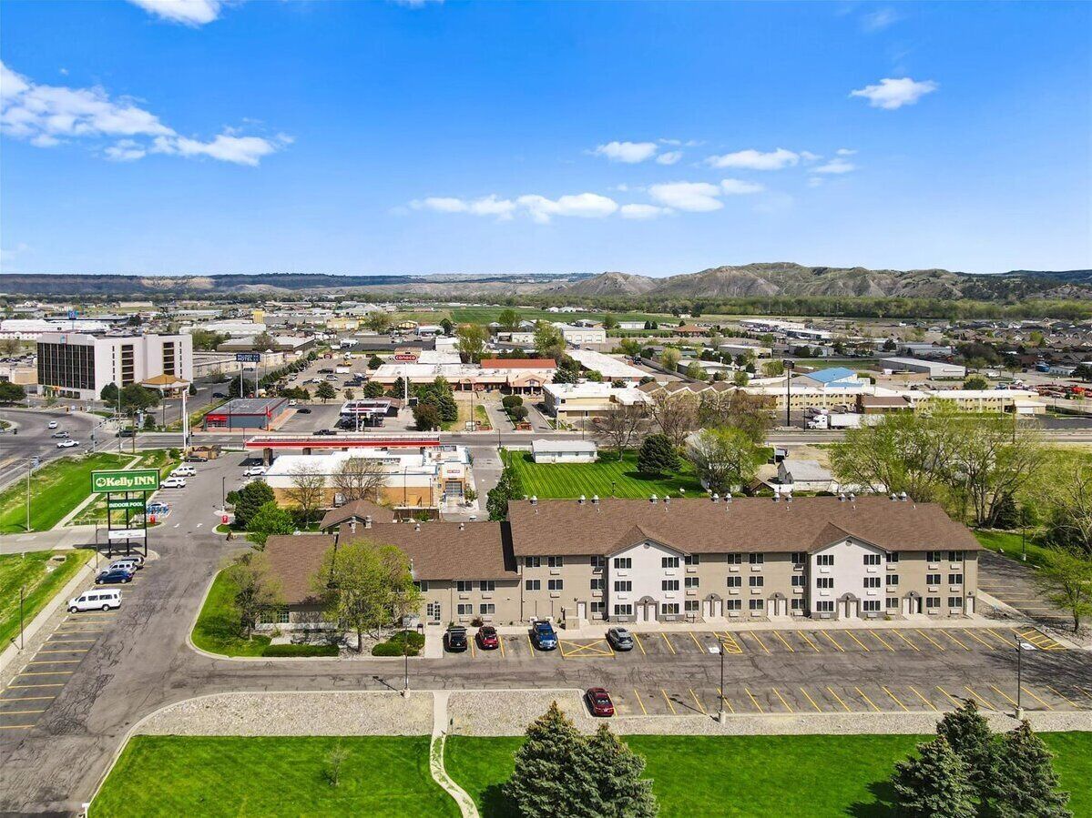 A multi-story hotel with a parking lot, surrounded by greenery and a clear sky.