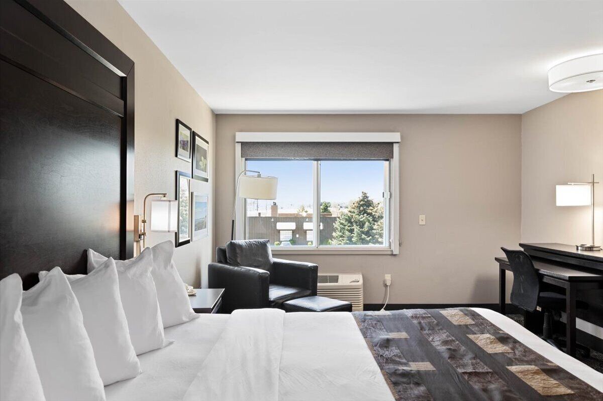 Habitación de hotel con una cama grande, un escritorio, una silla y una ventana que da a edificios.