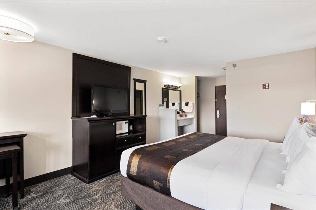 A hotel room with a large bed, a desk, a television, a mirror, and a small kitchenette.