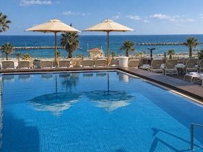 A pool area with lounge chairs and umbrellas, overlooking a beach and ocean. - Orchid Tel Aviv (Tel Aviv)
