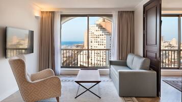 Una habitación de hotel moderna con un ventanal grande, un sofá, una silla y una mesita.