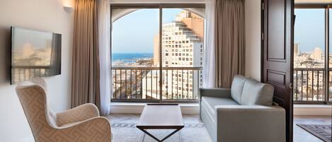 A modern hotel room with a large window, a sofa, a chair, and a small table.