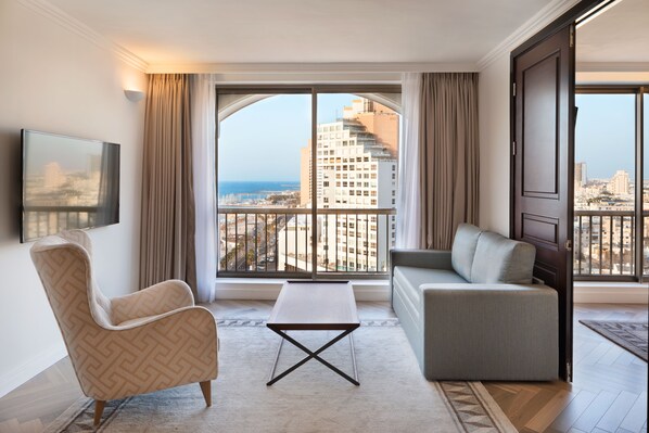 Una habitación de hotel moderna con un ventanal grande, un sofá, una silla y una mesita.