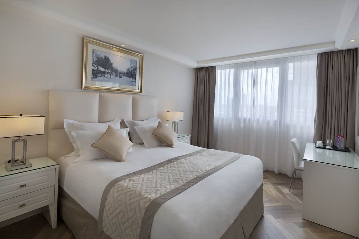 A hotel room with a large bed, bedside tables with lamps, a desk, and a chair.