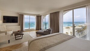 A spacious hotel room with a large bed, a sofa, a TV, and a view of the beach and ocean. - Orchid Tel Aviv (Tel Aviv)