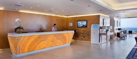 Una zona de recepción moderna con un mostrador de madera, un televisor y vista al mar.