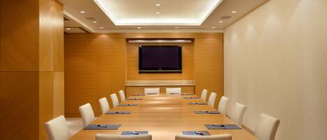 Une salle de conférence avec une longue table, des chaises blanches et un grand écran à l’avant.