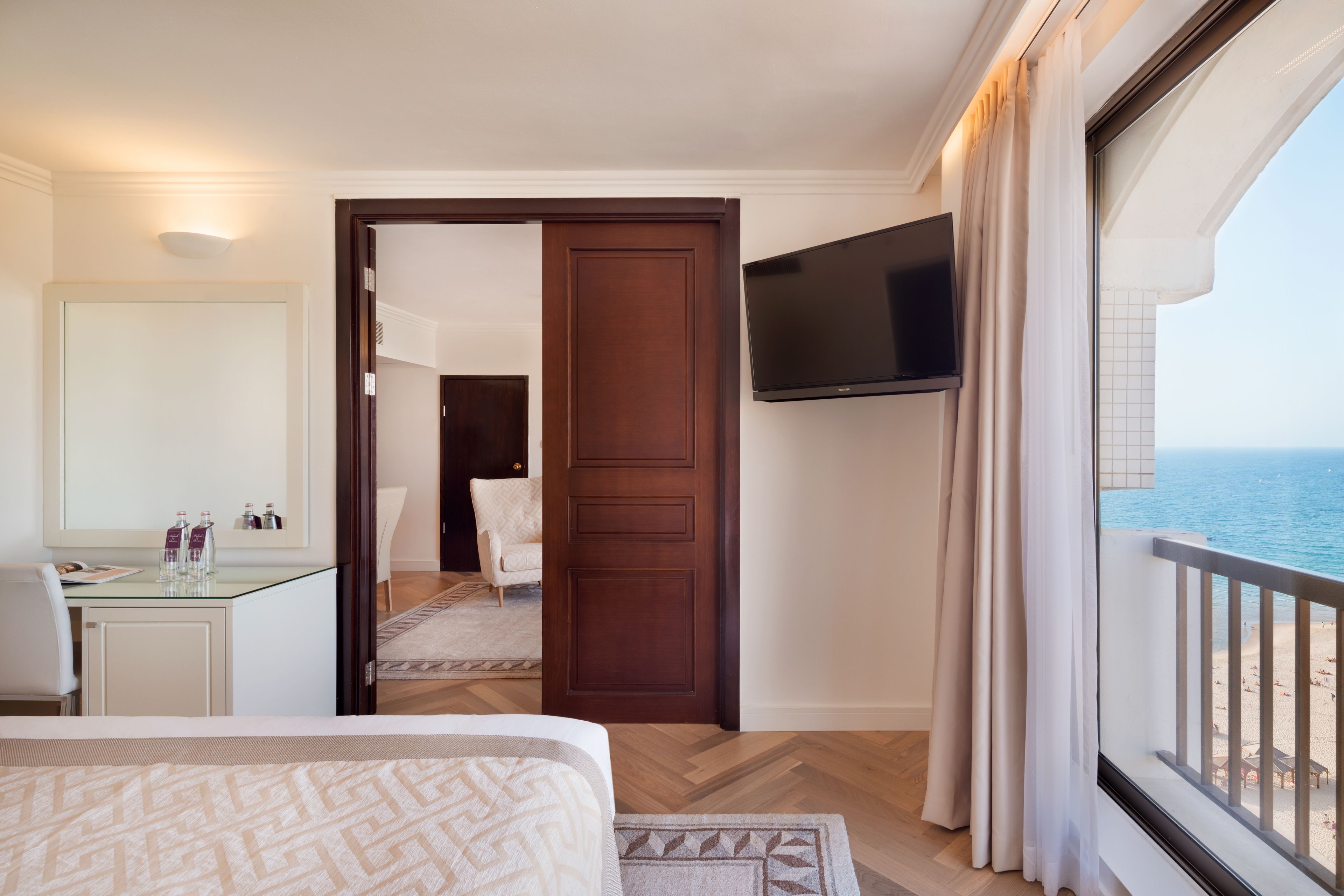 A hotel room with a bed, a desk, a TV, and a view of the ocean.
