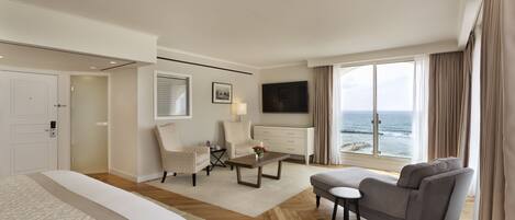 Une chambre d’hôtel avec un lit, un canapé, une chaise, une petite table, un téléviseur et une vue sur l’océan.