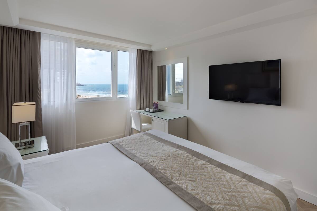 A hotel room with a bed, a desk, a TV, and a window with a view of the ocean.
