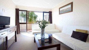 Una sala de estar moderna con un televisor de pantalla plana, un sofá blanco, una mesa de centro y un amplio ventanal con cortinas.