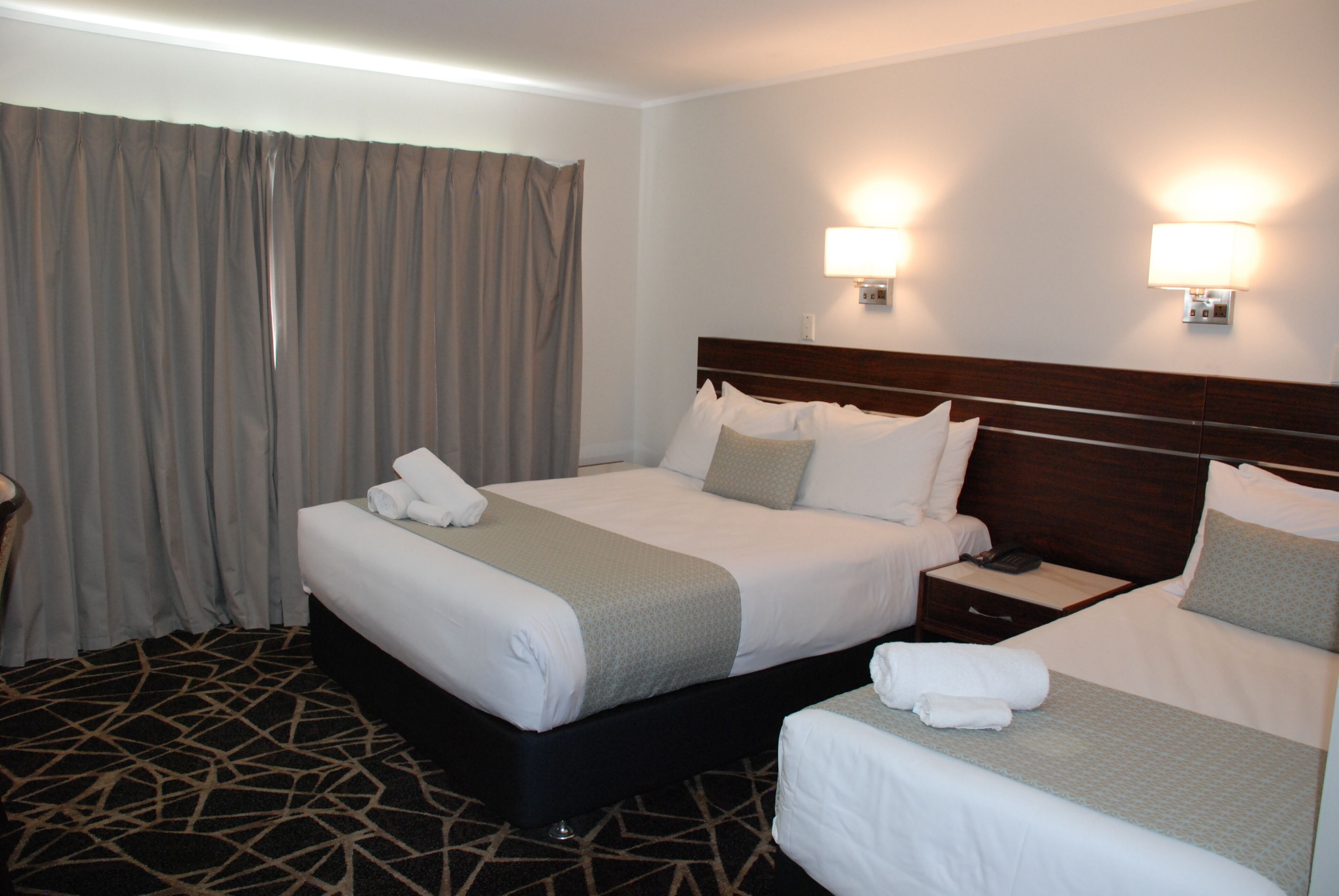 A hotel room with two beds, a nightstand, and a lamp.
