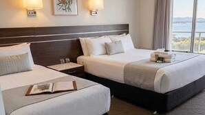 Habitación de hotel con dos camas, una mesita de noche, una lámpara, un cuadro enmarcado y vista al mar.