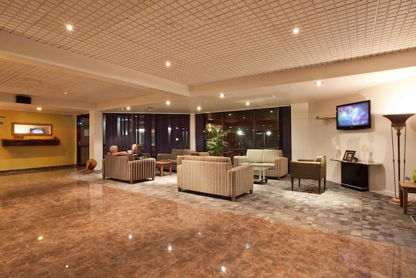 A spacious lobby with a marble floor, multiple seating areas, a flat-screen TV, and a reception desk.