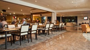 Un amplio vestíbulo de hotel con varias mesas y sillas para comer, una zona de recepción y una pantalla de televisión.