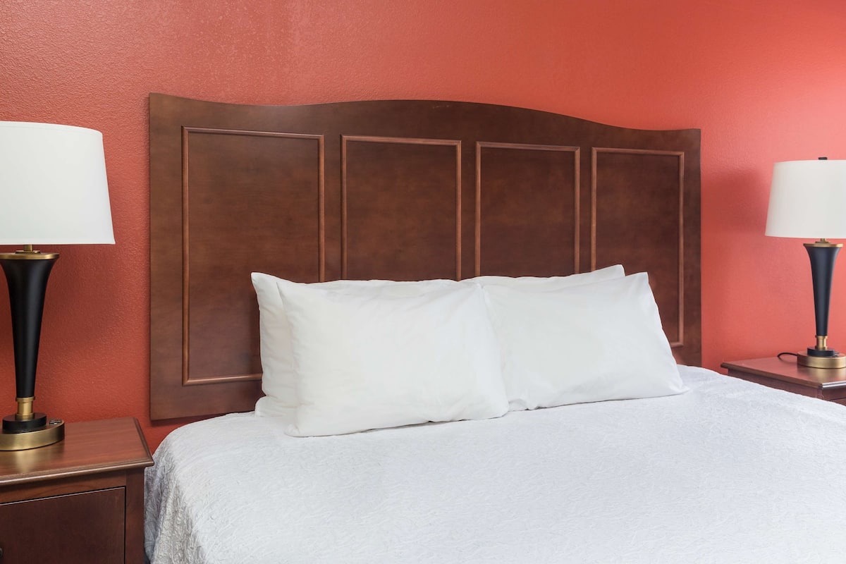Una cama bien hecha con sábanas y almohadas blancas, flanqueada por dos mesitas de noche con lámparas.
