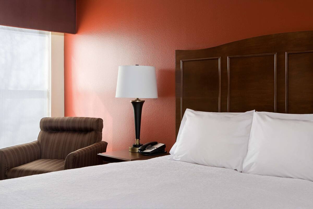 Una habitación de hotel con una cama, una silla, una lámpara y un teléfono sobre una mesita de noche.