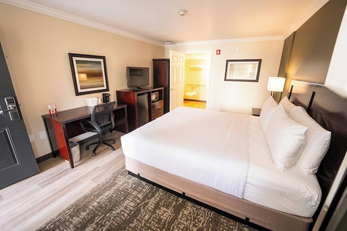 Ein Hotelzimmer mit einem großen Bett, einem Schreibtisch mit Stuhl, einem Fernseher und einer Tür zu einem Badezimmer.