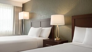 A hotel room with two beds, a headboard, bedside tables, lamps, and a window with curtains.