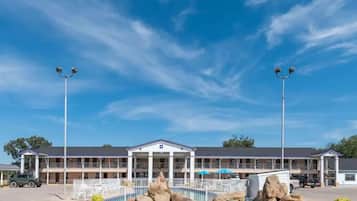 A motel with a pool area, large rocks, and a clear blue sky.