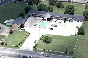 Vue aérienne d’un hôtel avec une piscine, un parking et des bâtiments adjacents.