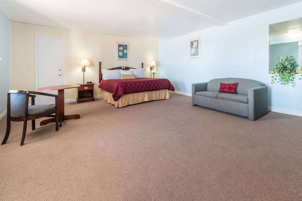A bedroom with a bed, a gray sofa, a wooden chair, a small table, and two wall-mounted lamps.