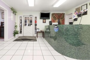 Una zona de recepción con mostrador de mármol, un televisor montado en la pared y una puerta con panel de vidrio.