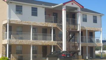 A multi-story building with a central staircase, balconies, and a car parked in front.