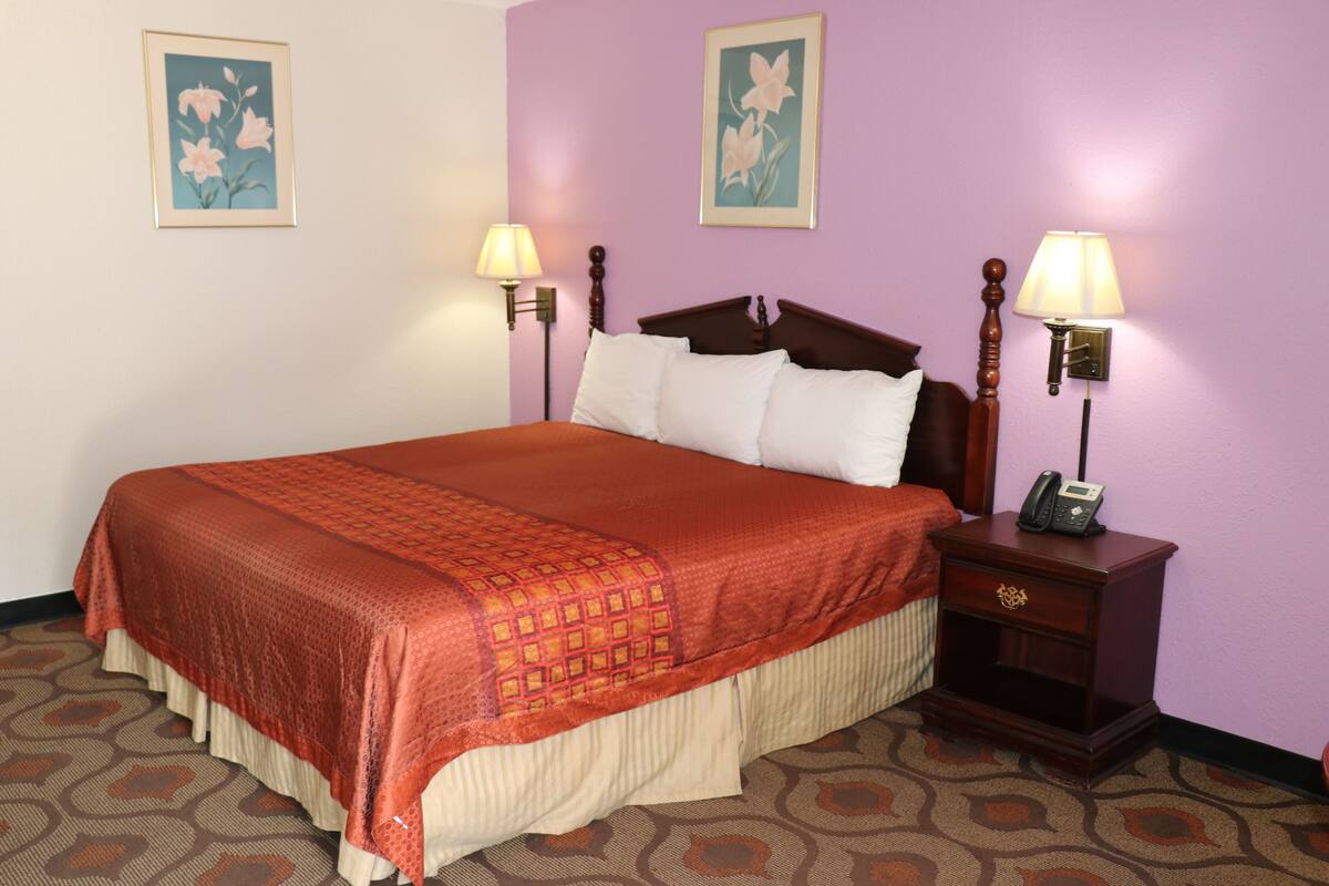 A neatly made bed with a red and beige bedspread, two bedside lamps, and a nightstand with a phone.