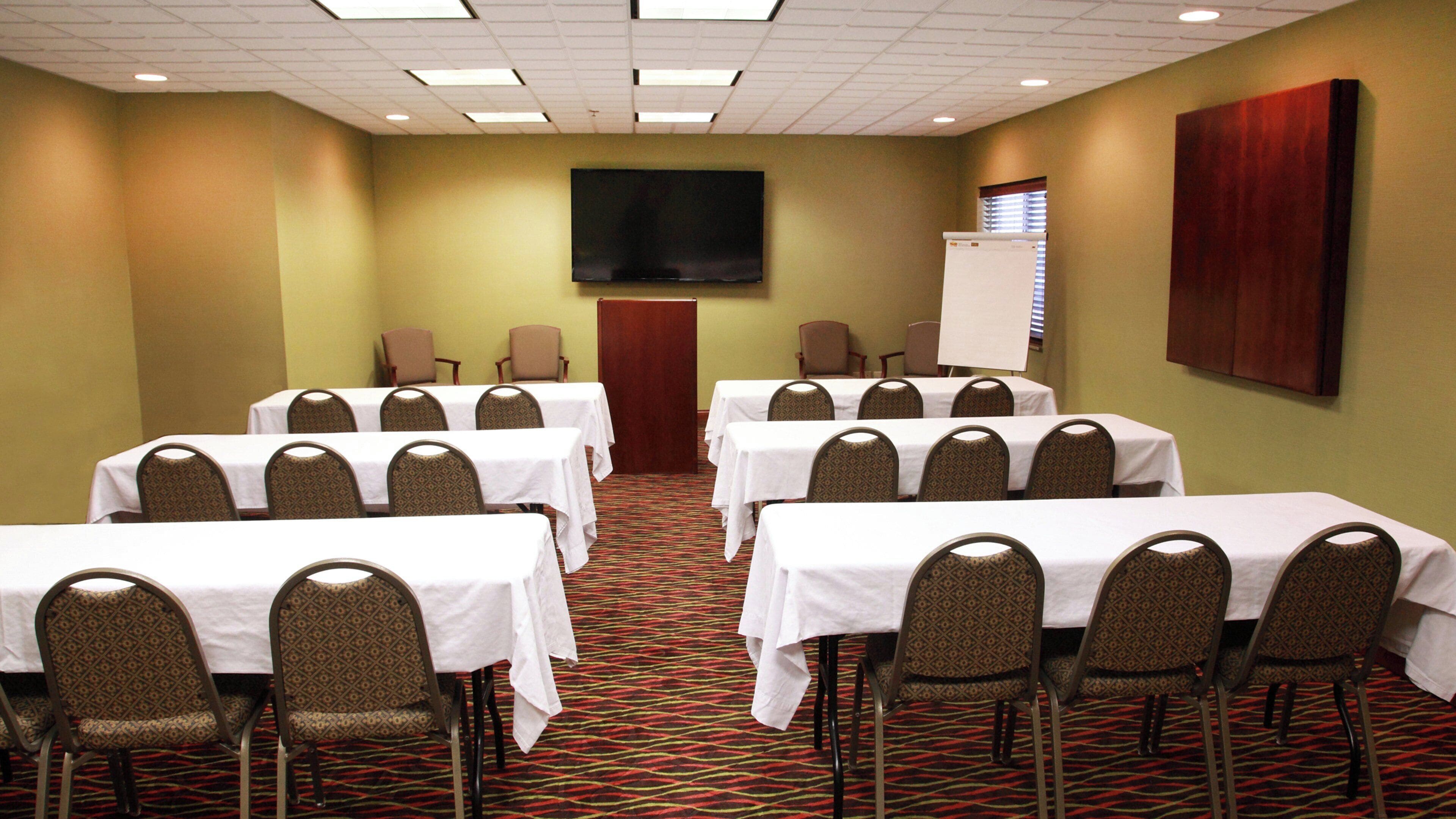 A conference room with multiple tables and chairs, a flat-screen TV, and a whiteboard.