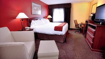 Ein Hotelzimmer mit einem Bett, zwei Nachttischlampen, einem Schreibtisch mit Computer, einem Sessel und einem Fernseher.