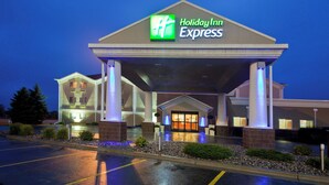 Edificio de Holiday Inn Express con entrada cubierta, estacionamiento y zona ajardinada con arbustos.