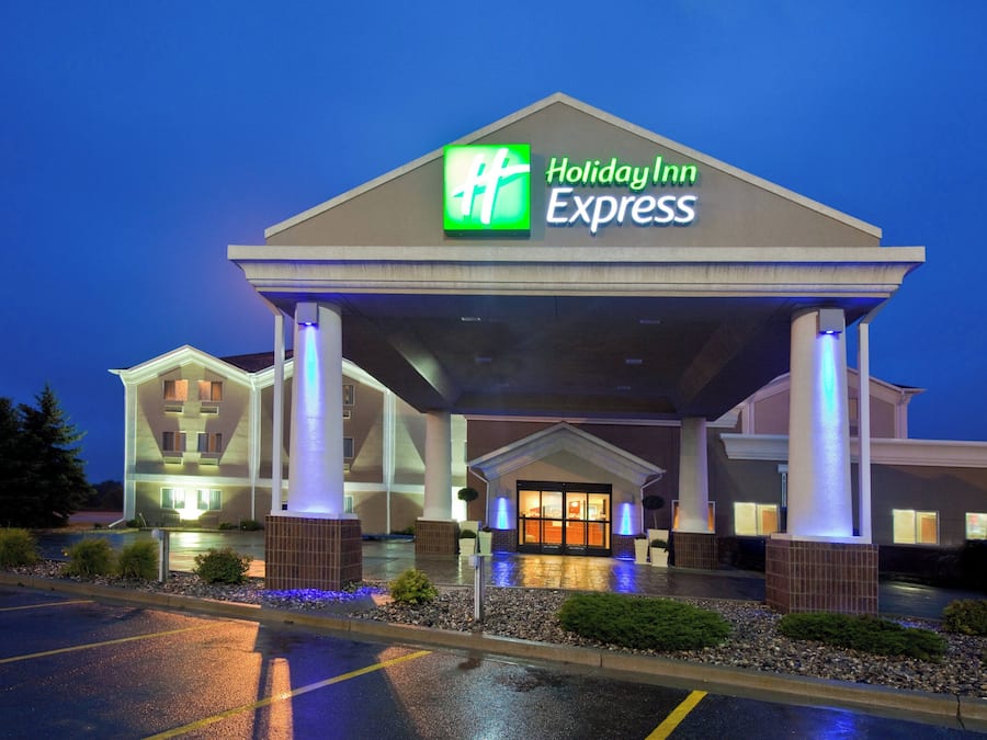 Un bâtiment de l’hôtel Holiday Inn Express doté d’une entrée abritée, d’un parking et d’un espace paysager agrémenté d’arbustes.